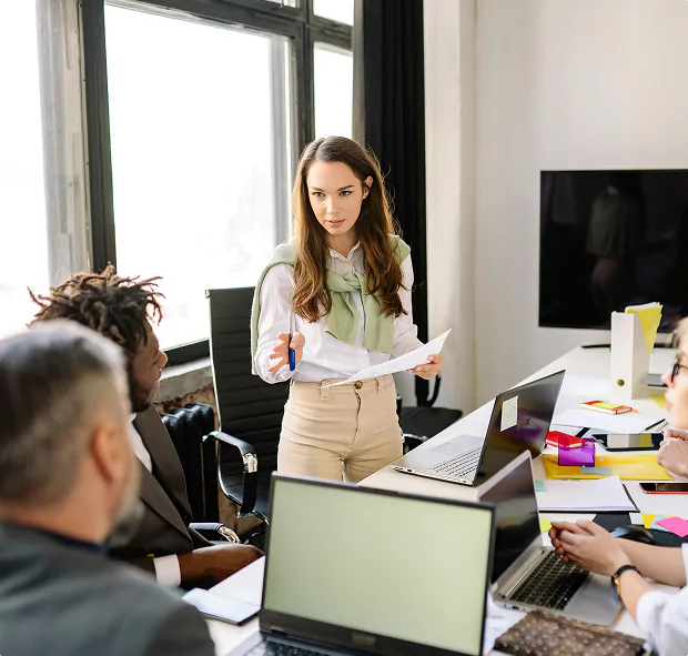 A woman leading a team meeting in a modern office with laptops and papers.
