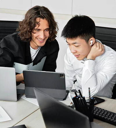 Two young professionals working together at a desk with multiple laptops and a tablet