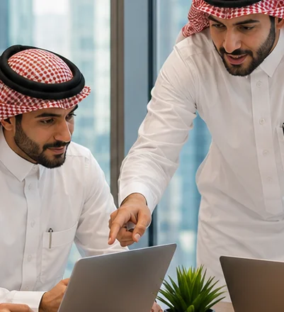 Two women in formal attire sit side by side in a meeting, one taking notes.